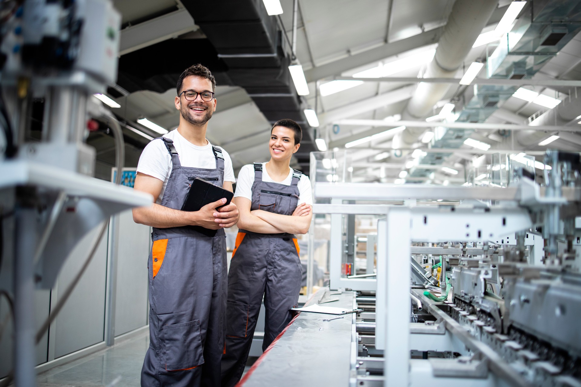 Retrato de los trabajadores de la línea de producción que controlan el proceso de fabricación de la máquina industrial de envasado moderna en la fábrica de impresión.